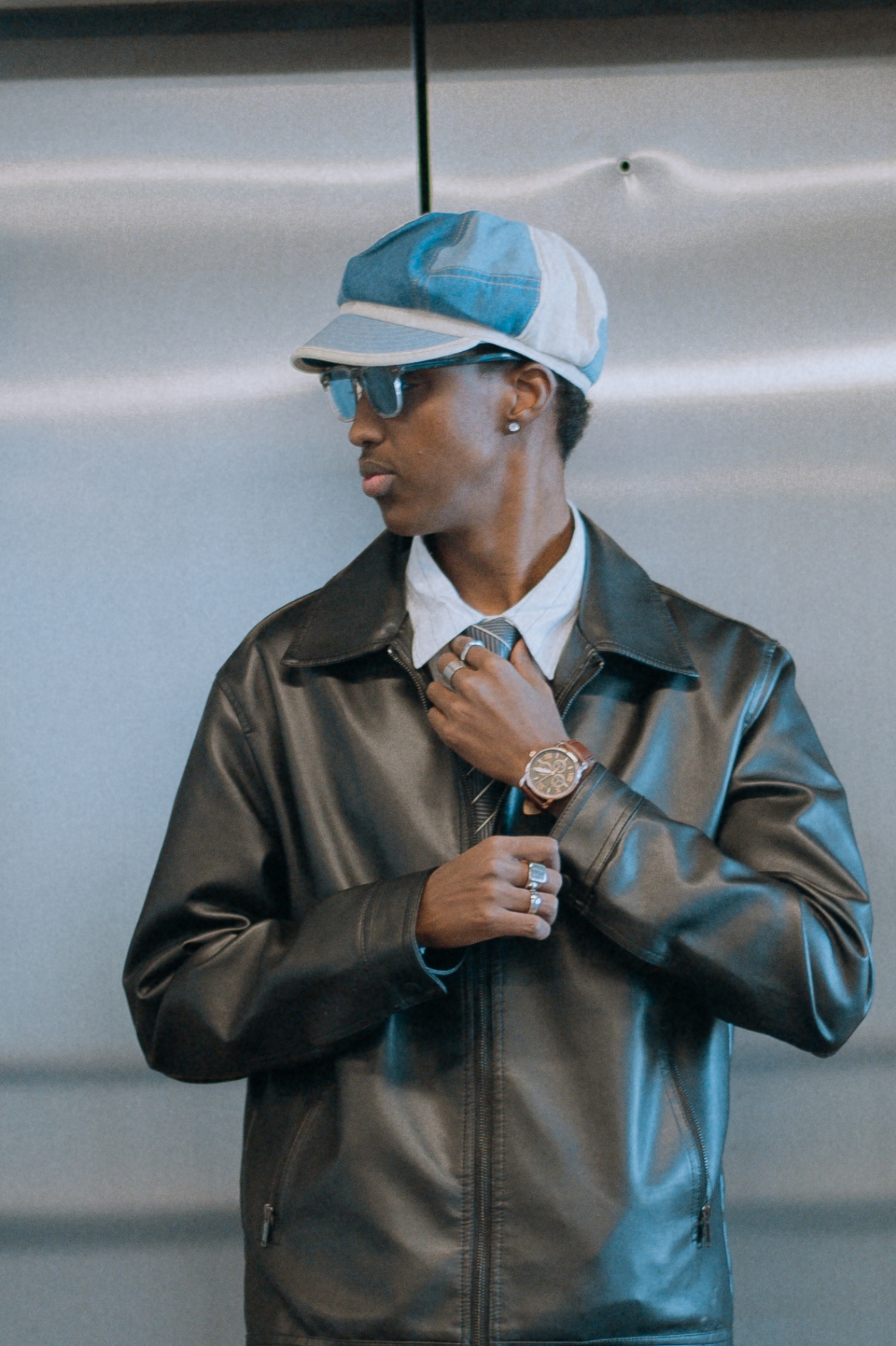 Portrait adjusting a tie in a leather jacket and denim cap